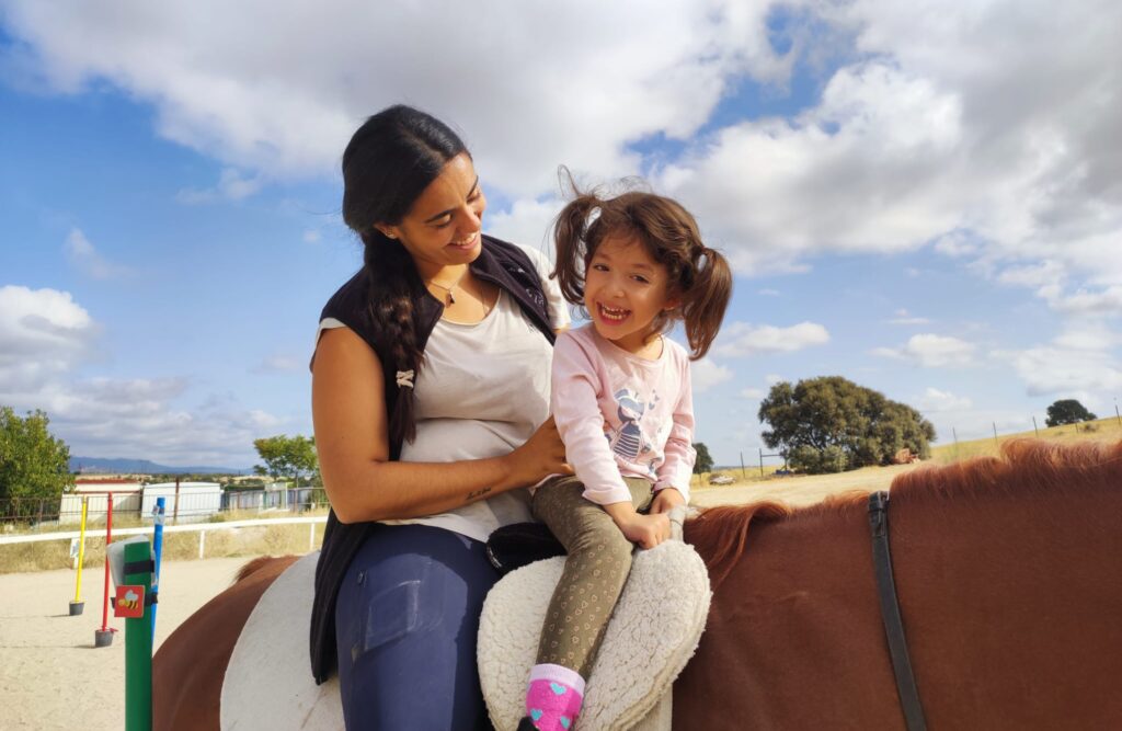 Fotografía de una niña y su terapeuta a caballo durante una sesión
